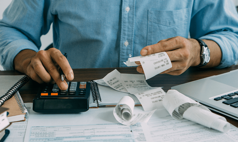 Person calculating expenses with receipts and calculator.