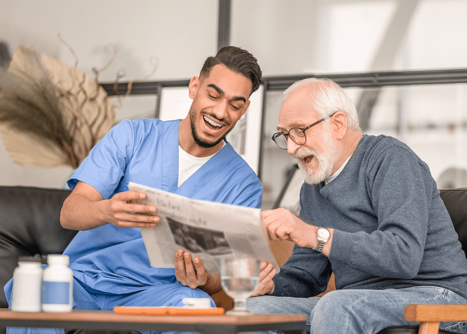 Caregiver and elderly man reading newspaper together.