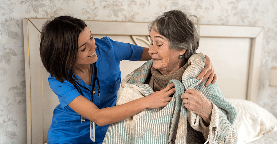 Caregiver assisting elderly woman with blanket.